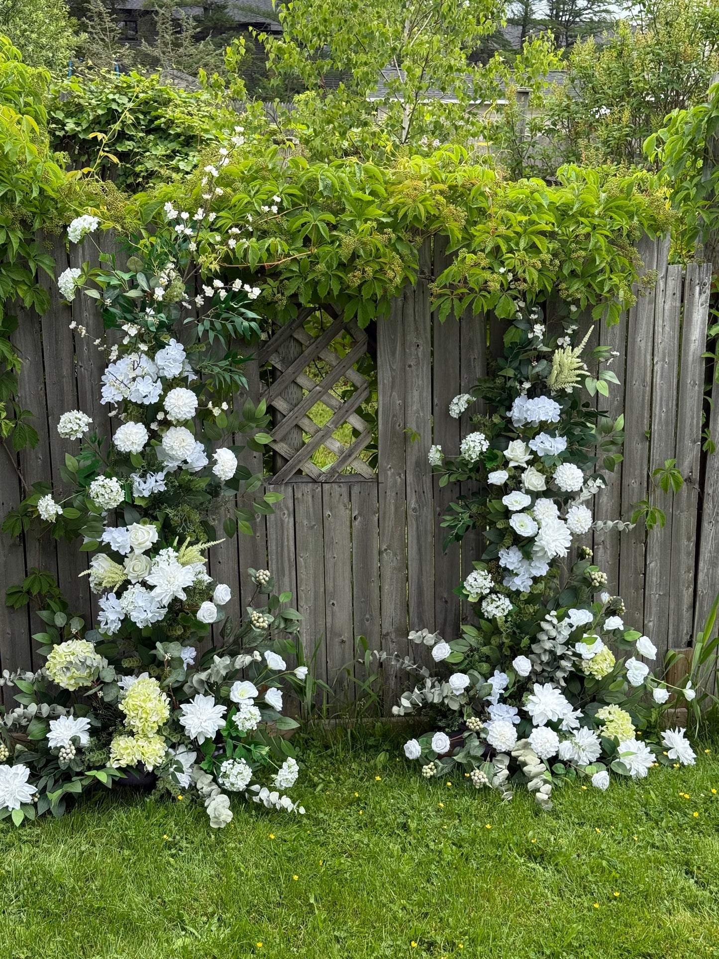 Floral broken arch on a wooden structure with greenery around with white flowers 